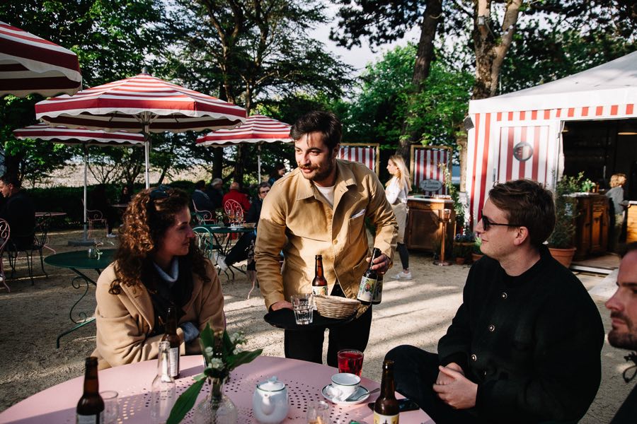 Un serveur apporte des bières à une table de la terrasse, parasols rayés en arrière-plan