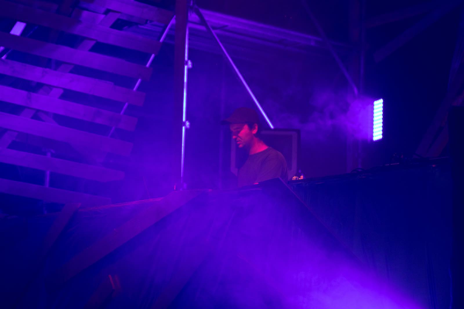 Un DJ derrière ses platines dans le hangar, noyé de fumée et de lumière violette